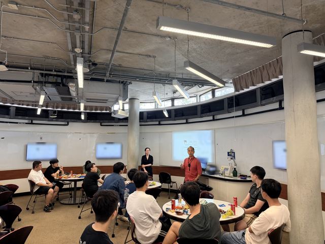 A guest speaker presenting in a lecture room while participants listen at tables